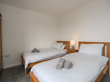 A bedroom with two single beds with white bedding and folded towels on top at Porth Ewyn in Trearddur Bay