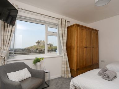 A bedroom with a wooden wardrobe a gray armchair and two beds with rolled towels at Porth Ewyn in Trearddur Bay