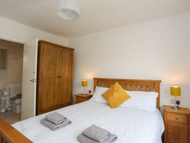 A bedroom with a wooden bed frame white bedding yellow pillows two wooden nightstands with lamps and a wooden wardrobe at Porth Ewyn in Trearddur Bay