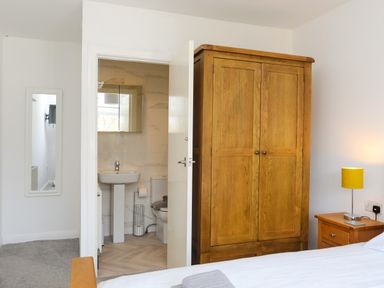 A bedroom with a wooden wardrobe a bedside table with a lamp and an open door leading to a bathroom at Porth Ewyn in Trearddur Bay