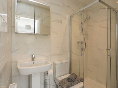 A bathroom with a pedestal sink a toilet with folded towels on top and a glass-enclosed shower at Porth Ewyn in Trearddur Bay