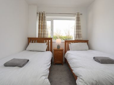 A bedroom with two single beds a wooden nightstand and a window with curtains at Porth Ewyn in Trearddur Bay