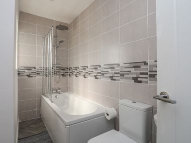 A bathroom with a bathtub shower combination toilet and tiled walls at Porth Ewyn in Trearddur Bay
