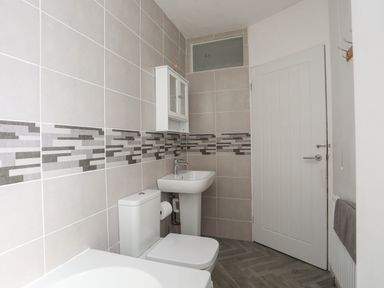 A bathroom with a toilet sink bathtub wall cabinet and tiled walls at Porth Ewyn in Trearddur Bay