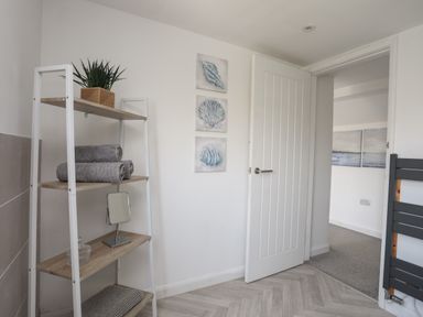 A bathroom with a wooden shelf holding towels a plant and a mirror and an open door showing a hallway at Porth Ewyn in Trearddur Bay