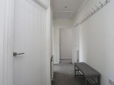 A hallway with a closed white door a gray bench along the wall and a row of hooks above the bench at Porth Ewyn in Trearddur Bay