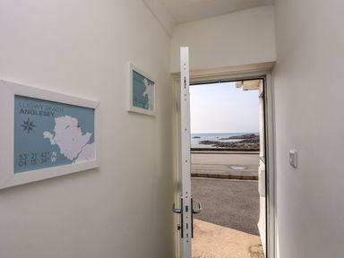A view from inside a building looking out through an open door onto a road and rocky shore with the sea beyond at Porth Ewyn in Trearddur Bay