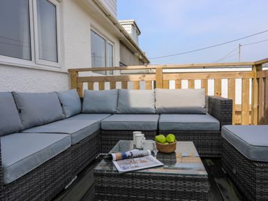An outdoor seating area with a sectional sofa a glass coffee table with mugs a basket of fruit and a magazine at Porth Ewyn in Trearddur Bay