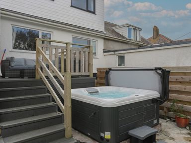 An outdoor area with a hot tub next to wooden stairs and a patio with seating at Porth Ewyn in Trearddur Bay