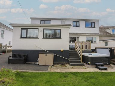 The rear view of a two-story house with a small patio area with stairs a hot tub a bench and a storage cabinet at Porth Ewyn in Trearddur Bay