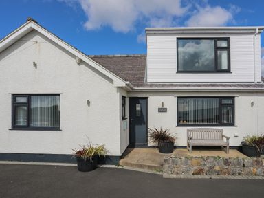 A white house with black framed windows a bench and potted plants at Porth Ewyn in Trearddur Bay