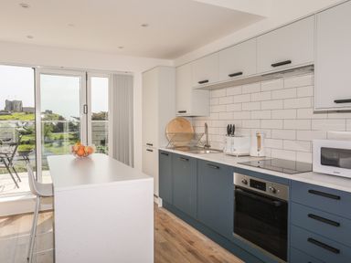 A kitchen with blue lower cabinets and white upper cabinets with a countertop and appliances at Golygfa'r Gastell Castle View in Criccieth
