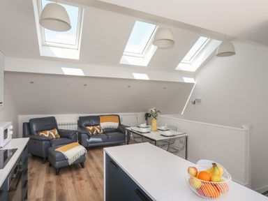 A living area with blue leather sofas dining table with chairs kitchen island and skylights at Golygfa'r Gastell Castle View Criccieth
