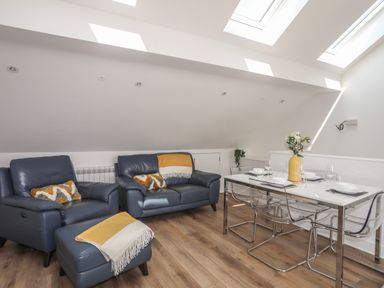 A living area with blue leather armchairs and a sofa with yellow and white blankets a dining table set with glassware and a yellow vase with flowers at Golygfa'r Gastell Castle View in Criccieth