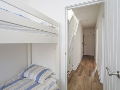 A hallway with wooden floors and white walls next to a room with a bunk bed with striped bedding at Golygfa'r Gastell Castle View in Criccieth