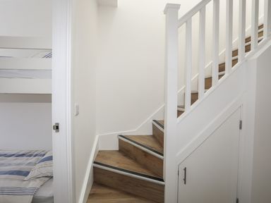A wooden staircase with white railings next to a small storage door and a bunk bed with striped bedding at Golygfa'r Gastell Castle View in Criccieth