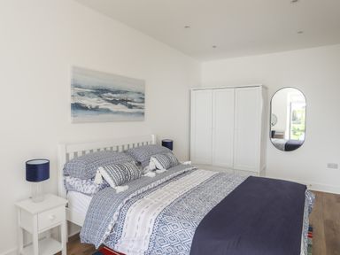 A bedroom with a bed dressed in patterned bedding a white nightstand with a lamp a white wardrobe and an oval mirror on the wall at Golygfa'r Gastell Castle View in Criccieth