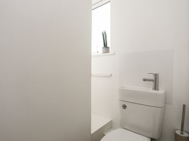 A small bathroom with a toilet that has a built-in faucet on the tank and a plant on the window sill at Golygfa'r Gastell in Criccieth