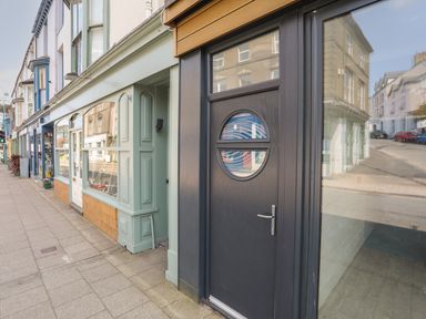 A street view with shopfronts and a dark door with round windows at Golygfa'r Gastell Castle View in Criccieth