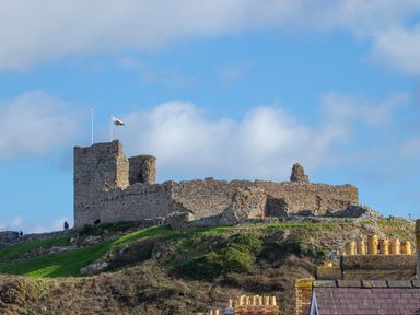 A stone castle ruin on a grassy hill with a flag flying at Golygfa'r Gastell Castle View in Criccieth