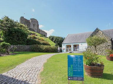 A stone castle on a hill with a cobblestone path leading to a stone building and a blue welcome sign in front at Golygfa'r Gastell Castle View in Criccieth