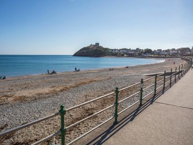 A pebble beach with a railing and a castle on a hill in the background at Golygfa'r Gastell Castle View in Criccieth
