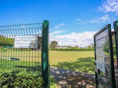 An open gate showing a green field and benches at Criccieth Bowling Club in Criccieth