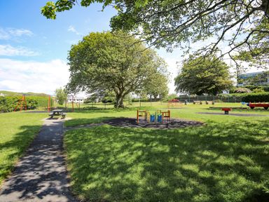 A playground with swings merry-go-round and picnic table surrounded by grass and trees at Golygfa'r Gastell Castle View in Criccieth