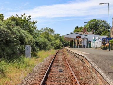 Railway tracks leading to a small station platform with a shelter and building surrounded by trees at Golygfa'r Gastell Castle View in Criccieth