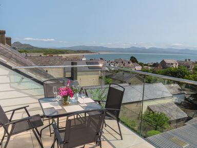 A balcony with a table and four chairs overlooking rooftops and a coastal landscape at Golygfa'r Gastell Castle View in Criccieth