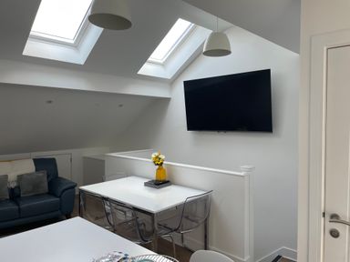 A dining area with a white table and transparent chairs next to a wall mounted TV in an attic room at Golygfa'r Gastell Castle View in Criccieth