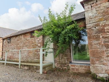Exterior view of a stone building with a wooden door and a large window next to a tree at The Courtyard in Kirklinton near Longtown