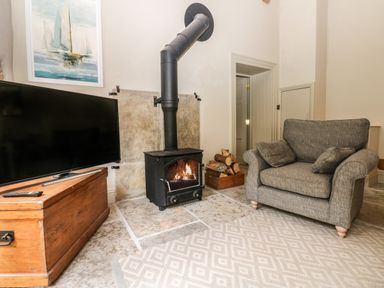 A living room with a wood burning stove gray armchair television and wooden chest at The Courtyard Kirklinton near Longtown