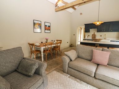A living room with gray sofas a dining table with four chairs and a kitchen with dark cabinets at The Courtyard in Kirklinton near Longtown