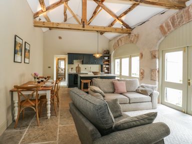 An open plan living and dining area with wooden beams a dining table with chairs and a kitchen with cabinets and an island at The Courtyard Kirklinton near Longtown