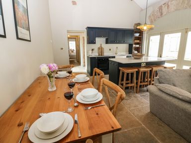 A kitchen and dining area with a wooden table set for four and a kitchen island with stools at The Courtyard in Kirklinton near Longtown