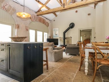 A living area with wooden beams a black kitchen island and dining table with chairs at The Courtyard in Kirklinton near Longtown
