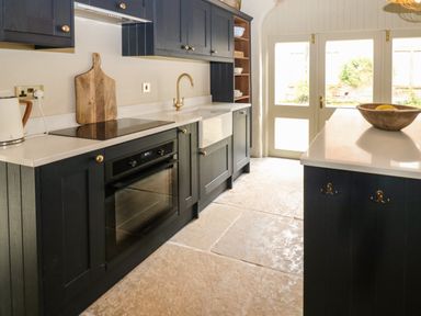 A kitchen with dark cabinets a built in oven a wooden cutting board and a sink at The Courtyard in Kirklinton near Longtown