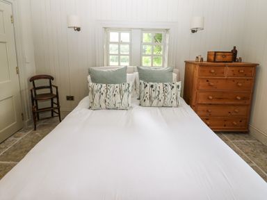 A bedroom with a bed with pillows a wooden chair and a wooden dresser at The Courtyard in Kirklinton near Longtown
