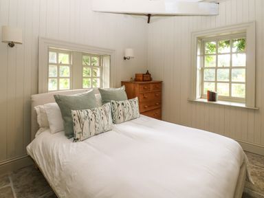 A bedroom with a bed pillows and a wooden dresser under windows at The Courtyard in Kirklinton near Longtown