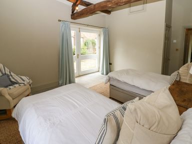 A bedroom with two single beds a wooden beam ceiling an armchair and glass doors with curtains at The Courtyard in Kirklinton near Longtown