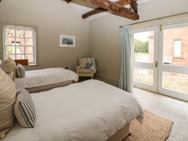 A bedroom with two beds a window an armchair and glass doors at The Courtyard in Kirklinton near Longtown