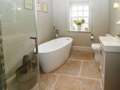 A bathroom with a freestanding bathtub a toilet a sink and a window with flowers at The Courtyard in Kirklinton near Longtown