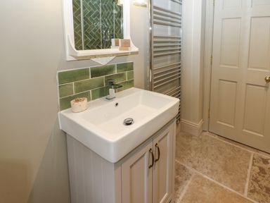 A bathroom sink with green tiles on the wall a mirror a towel rack and a door at The Courtyard in Kirklinton near Longtown