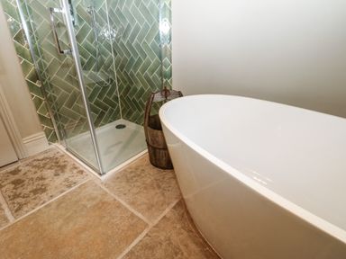 A bathroom with a freestanding bathtub and a glass shower with green tiles at The Courtyard in Kirklinton near Longtown