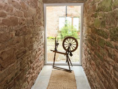A narrow stone hallway with a wooden spinning wheel in front of a glass door at The Courtyard in Kirklinton near Longtown