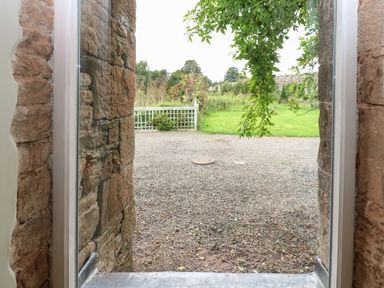 A view through a stone doorway onto a gravel path and green garden at The Courtyard in Kirklinton near Longtown