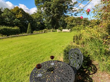 A garden with a metal table and two glasses of red wine on it and garden chairs in the background at The Courtyard in Kirklinton near Longtown