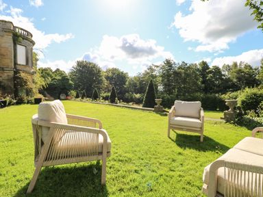 Outdoor seating with cushioned chairs on grass near a stone building and landscaped garden at The Courtyard in Kirklinton near Longtown