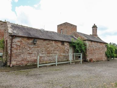 An old stone building with a slate roof a wooden ramp and a chimney at The Courtyard in Kirklinton near Longtown